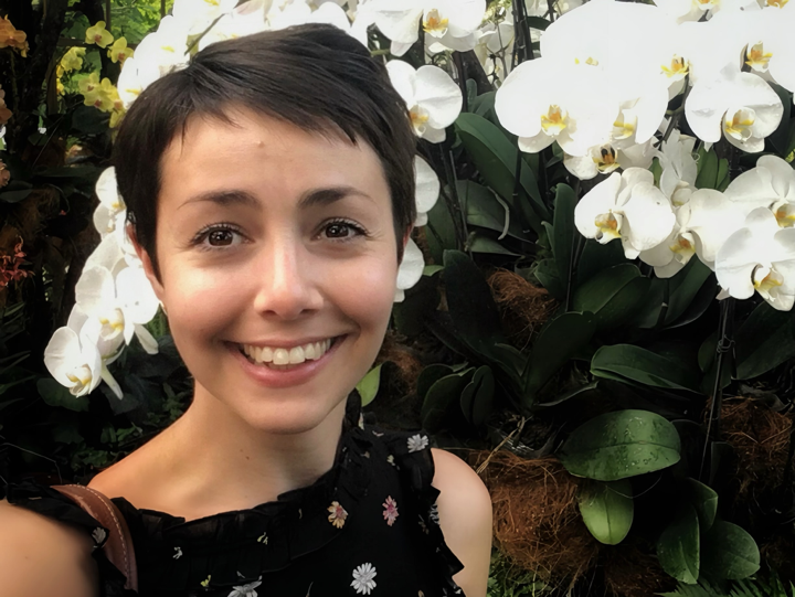 A woman with short, dark hair smiling in front of white orchids.